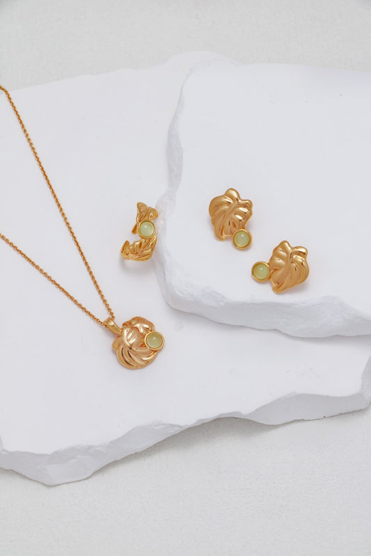 Gold jewelry set with leaf designs on a white fabric background