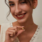 Woman holding a gold necklace with a cube pendant against a neutral background