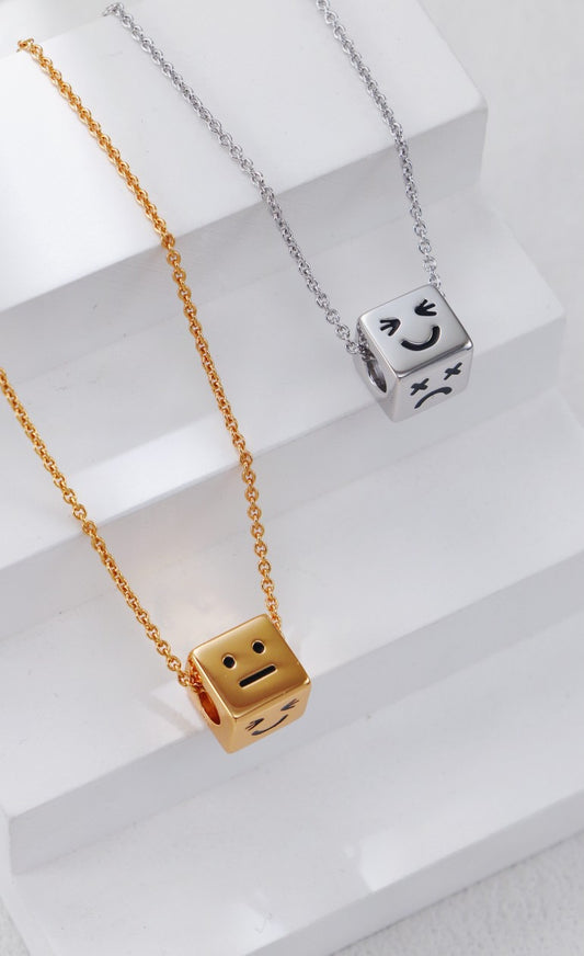 Gold and silver cube-shaped pendants on chains with a white background